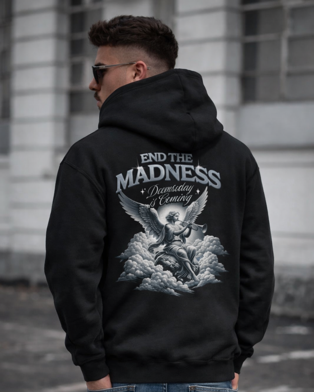 Person wearing a black hoodie with a graphic design and text on the back, standing against a building.