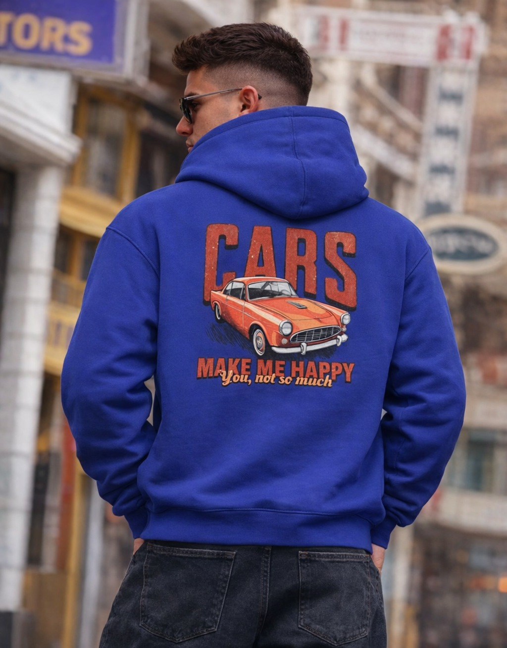 Person wearing a blue hoodie with a car graphic and text on the back, standing in an urban setting.