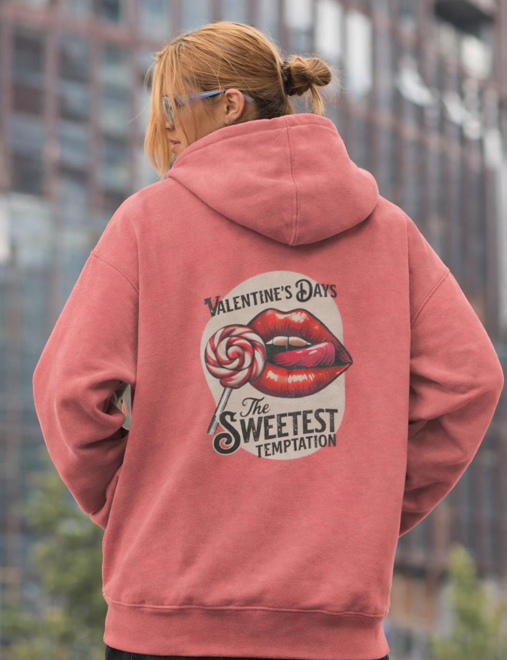 Person wearing a pink hoodie with a graphic design on the back, standing in an urban setting.